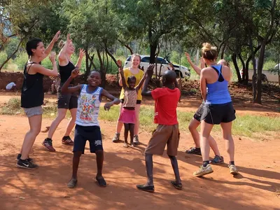 Volunteers dancing with children on red earth outdoors