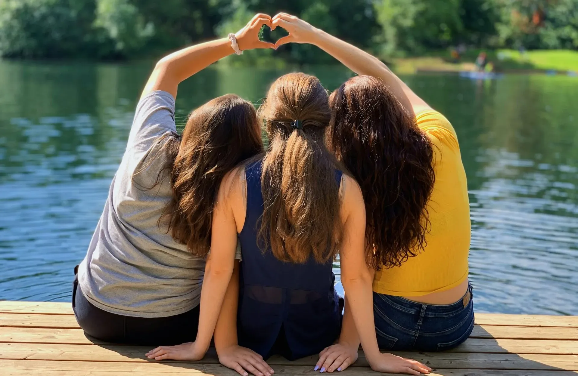 Three friends sitting on a jetty making a heart shape with their arms