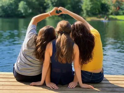 Three friends sitting on a jetty making a heart shape with their arms