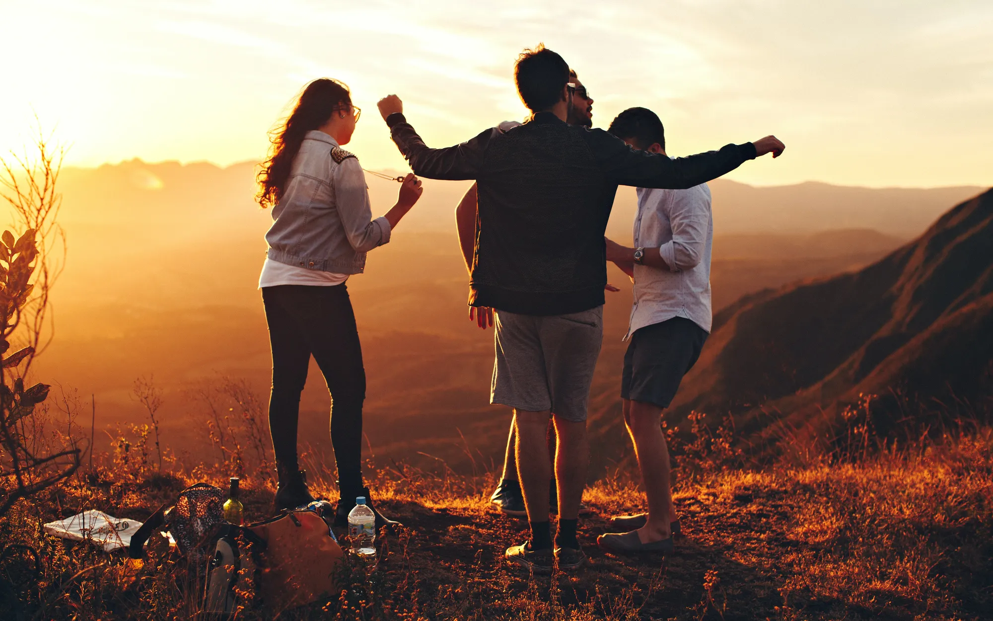 Three friends with arms outstretched watching the sunset over the mountains
