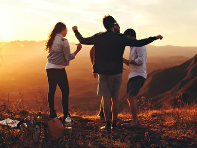 Three friends with arms outstretched watching the sunset over the mountains