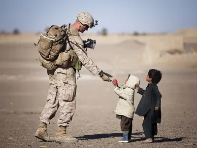 Soldier offering a gift to two small children in a dusty landscape