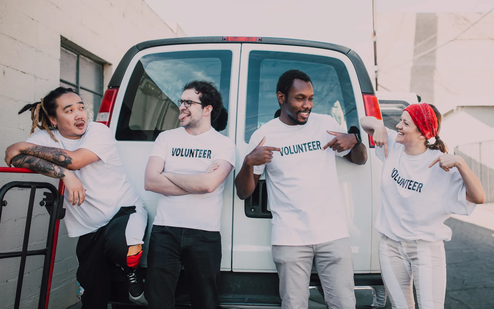 Four volunteers in Volunteer T-shirts laughing in front of a white van