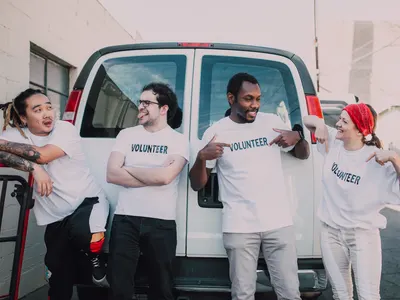 Four volunteers in Volunteer T-shirts laughing in front of a white van