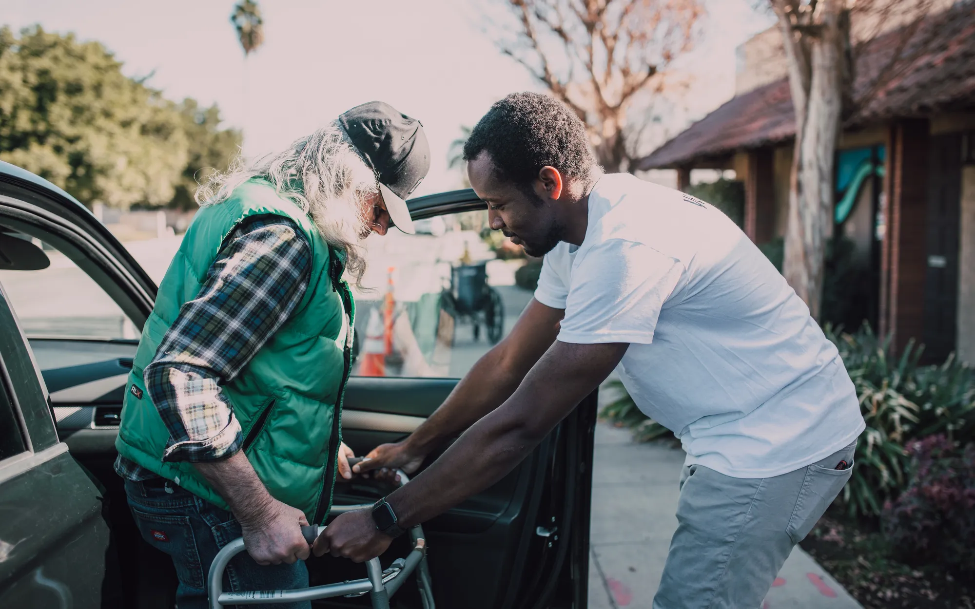 Volunteer helping an elderly man with a walking frame out of a car