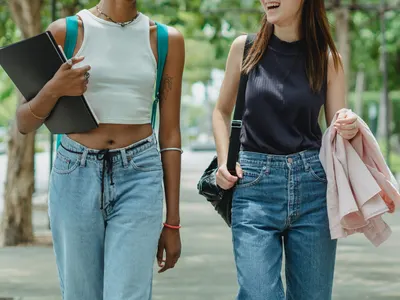 Two students walking side by side carrying folders and bags