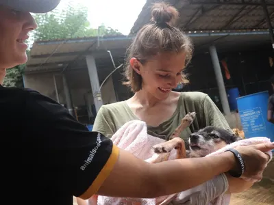 Smiling volunteer holding a small dog wrapped in a towel at an animal shelter